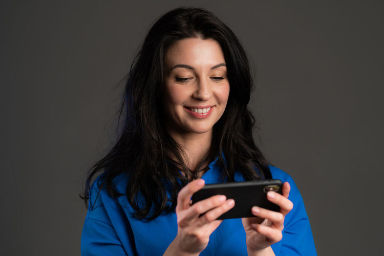 Smiling young woman using smart phone against black background