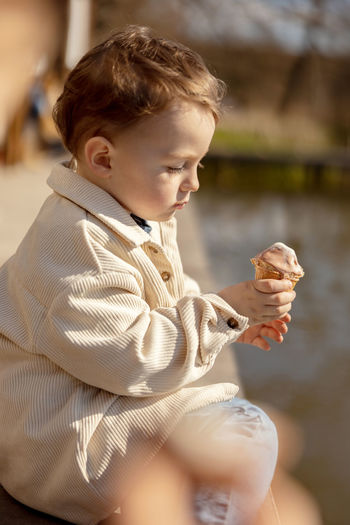 Little adorable boy sitting outdoors and eating ice cream. lake, water and sunny weather. 