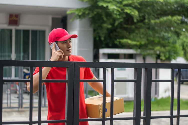 Delivery man standing at closed gate against buildings