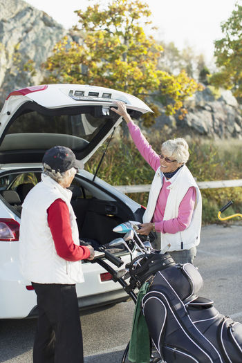 Senior female friends loading golf bag into car boot