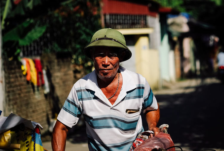 Portrait of vendor with bicycle wearing hat standing outdoors