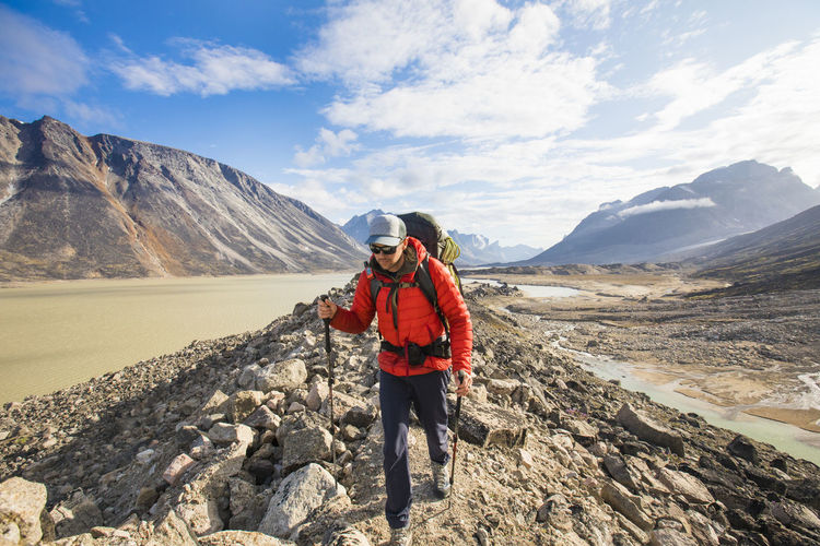 Backpacker wearing warm red jacket hiking over rugged terrain.