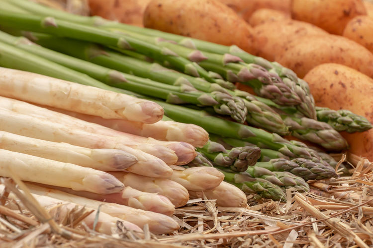Fresh raw organic green and white asparagus and potatoes on straw background. asparagus officinalis