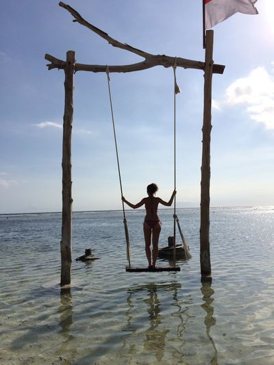 Full length rear view of woman standing on swing over sea against sky