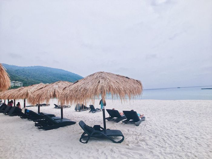 Lounge chairs and parasols at beach against sky