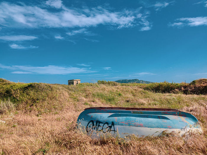Abandoned boat on field against blue sky
