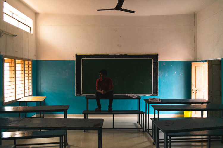 Teenage boy sitting on table against blackboard in school