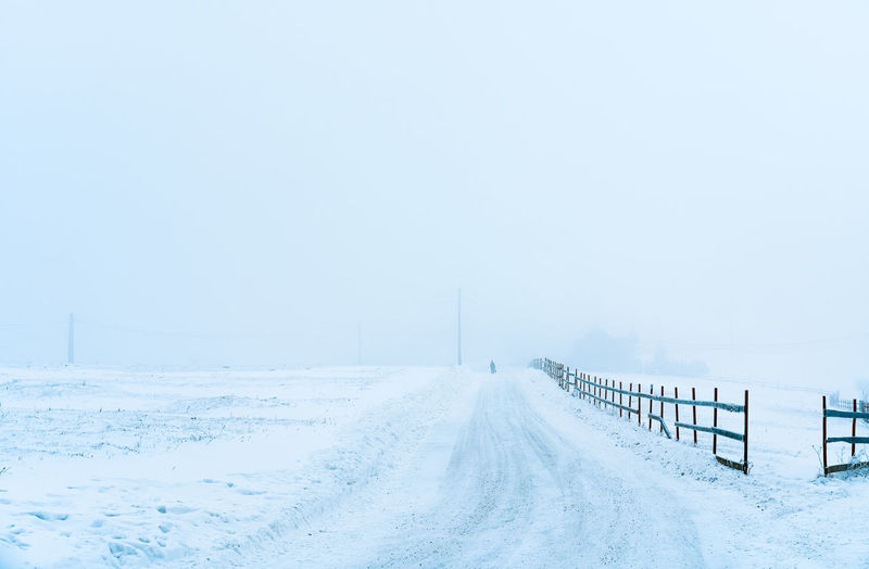 Scenic view of person walking on snow covered road in rural area in a foggy winter day