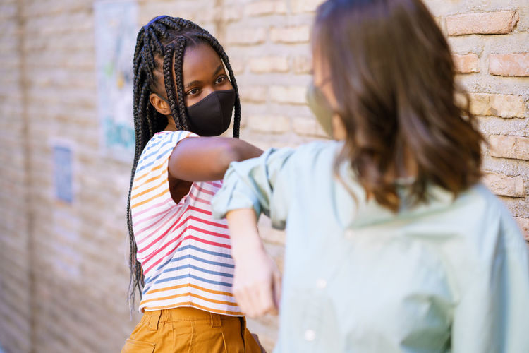 Young women wearing mask doing elbow bump outdoors