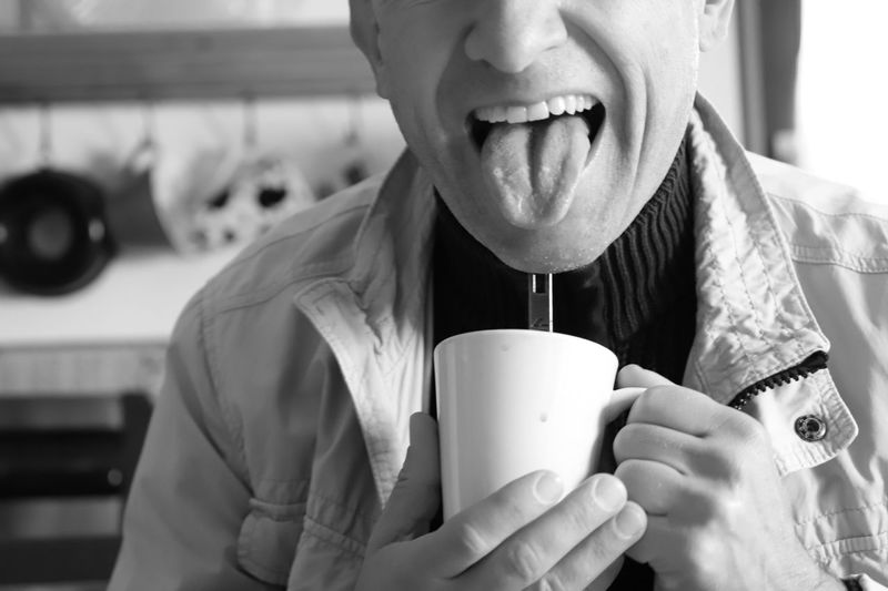 Midsection of man sticking out tongue while having coffee in cup