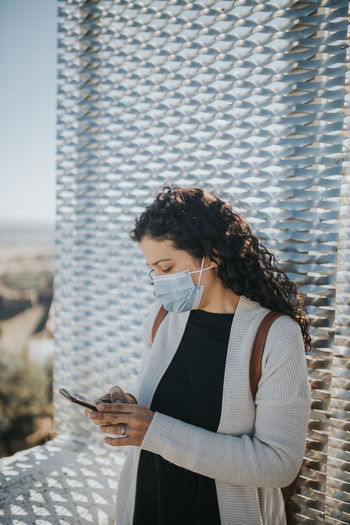 Side view of young woman using mobile phone with mask
