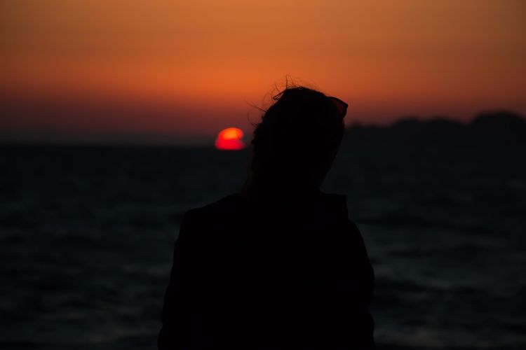 Silhouette woman standing at beach against sky during sunset