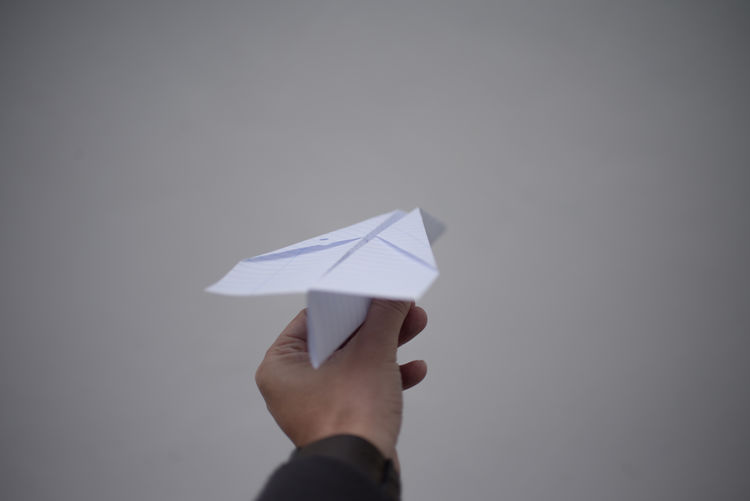 Cropped hand holding paper airplane against gray background