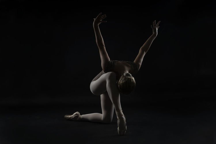 Ballet dancer stretching exercising against black background