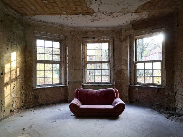 Interior of abandoned house with bis windows, light reflection on a wall and a sofa