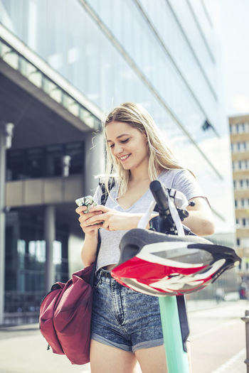 Portrait of young woman using mobile phone while standing in city