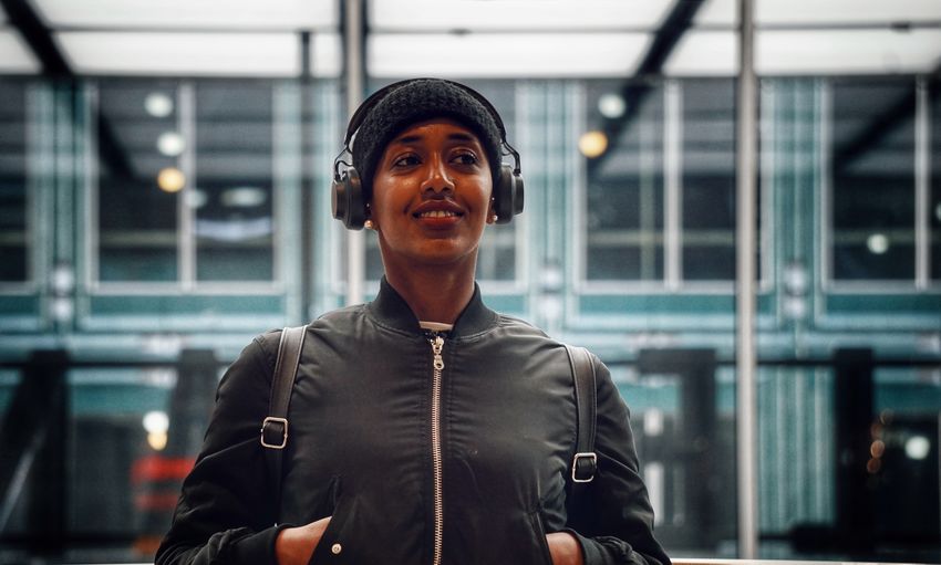 Smiling young woman wearing headphones while standing in building