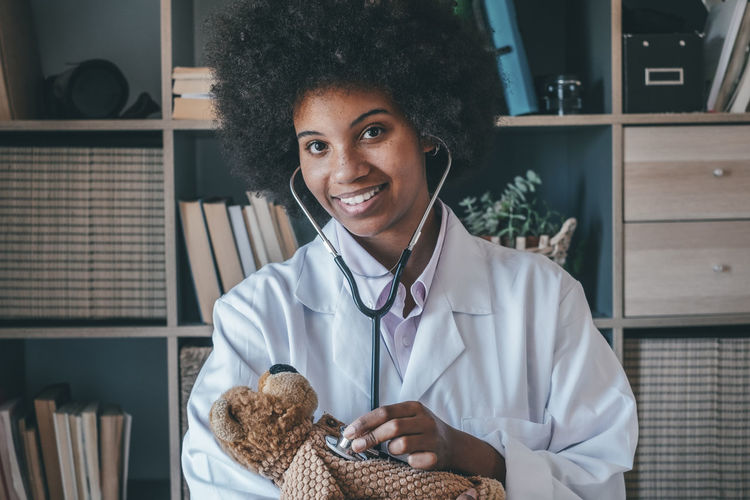 Portrait of smiling doctor examining stuffed toy at clinic