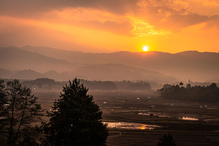 Sunrise over mountains with country side farming fields and orange dramatic sky at dawn at village