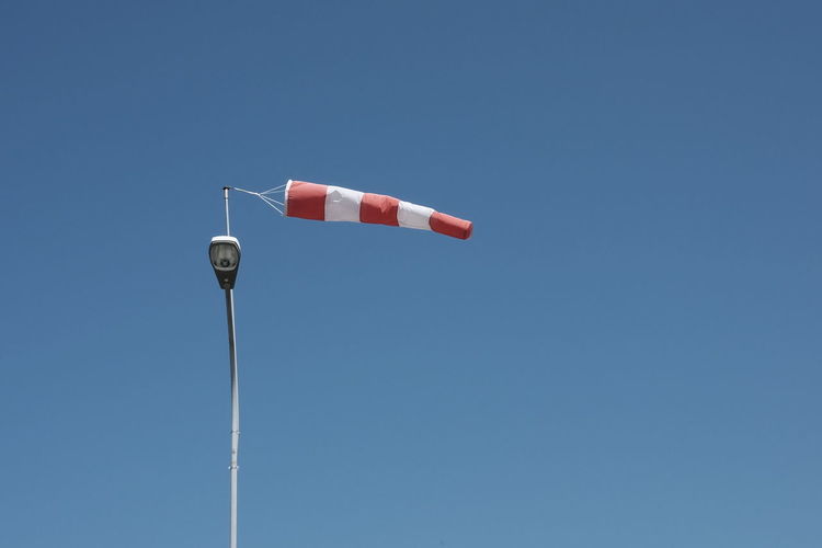 Low angle view of windsock hanging on street light against clear blue sky
