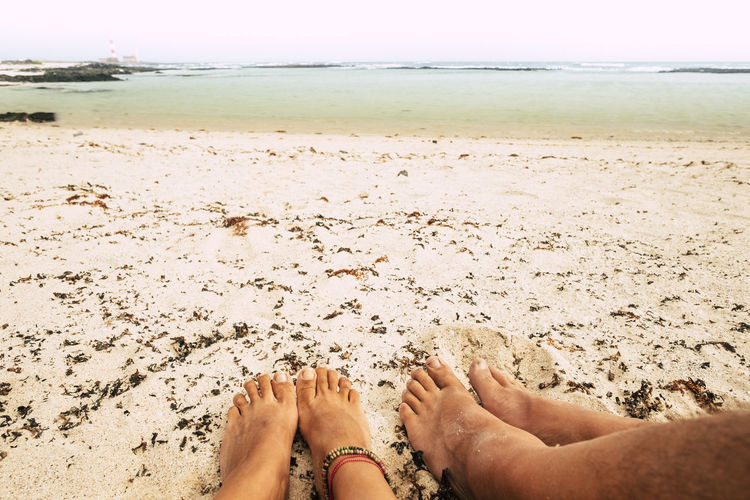 Low section of couple relaxing at sandy beach