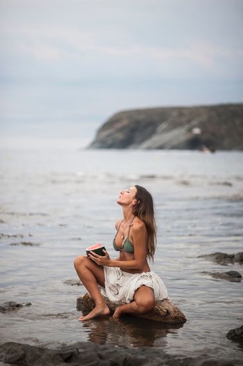 Woman holding watermelon while sitting on beach