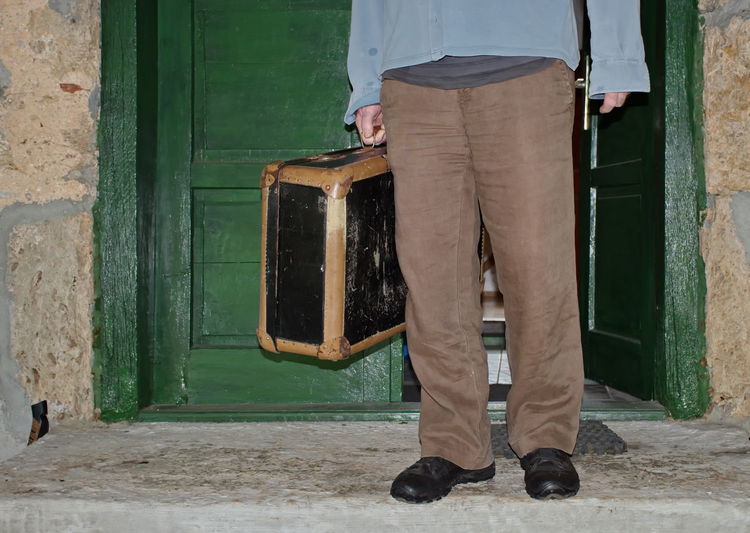 Midsection of man standing in the doorway with vintage suitcase