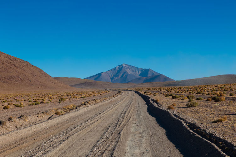 Dirt road amidst desert against blue sky