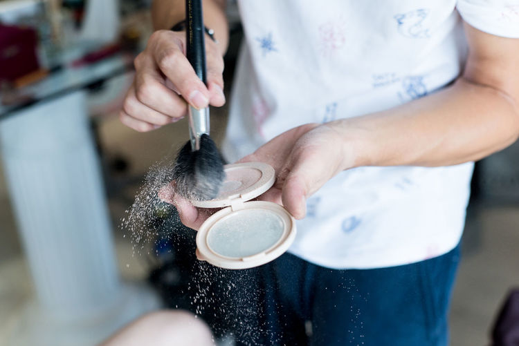Midsection of make-up artist holding compact powder and brush