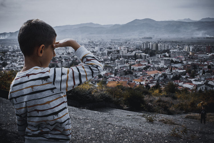Rear view of boy standing on city against cityscape