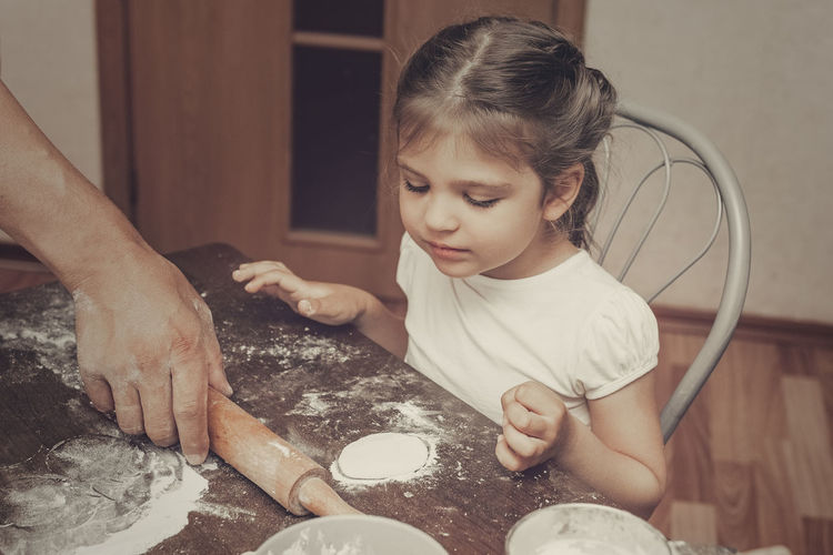 Cropped hand of father holding rolling pin preparing food with daughter