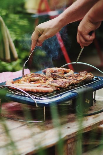 Man making barbecue meat pork stak and sausages on blue electric barbecue in the garden