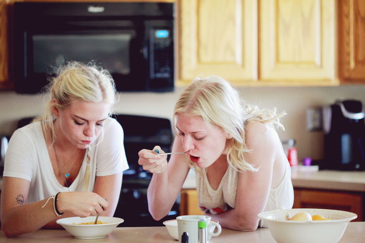 Sisters eating breakfast on table in kitchen