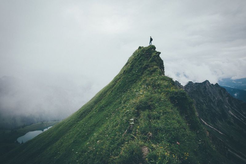 Man standing on mountain peak against cloudy sky