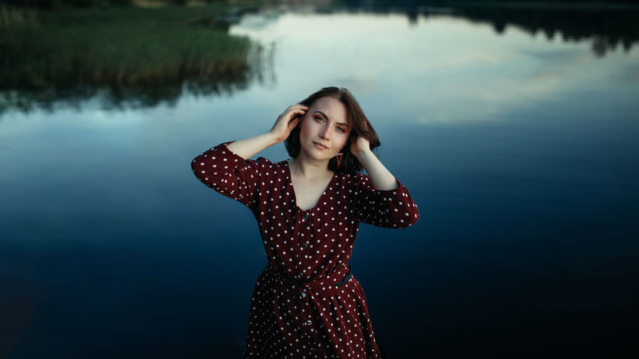 Portrait of beautiful young woman standing by lake