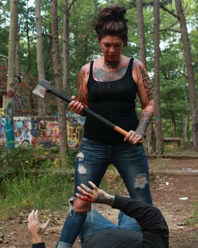 Woman holding axe standing over man in forest