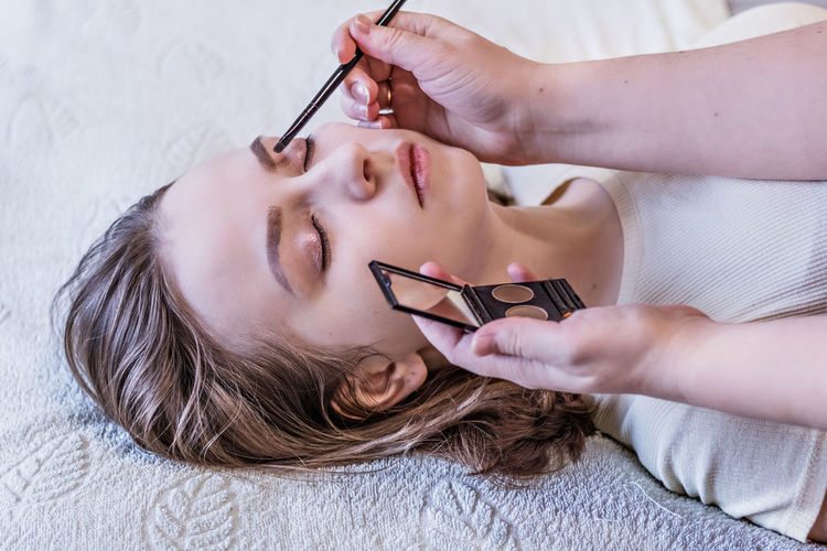 Cropped hands applying eyeshadow to woman