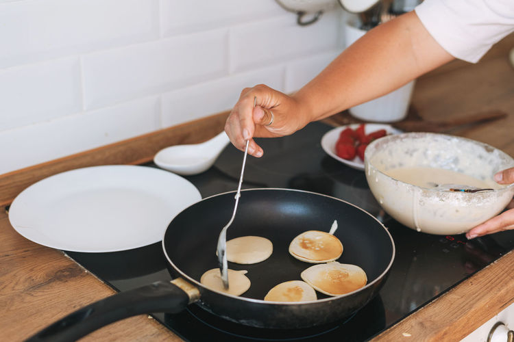 Young woman cooks pancakes in a frying pan in the kitchen at home