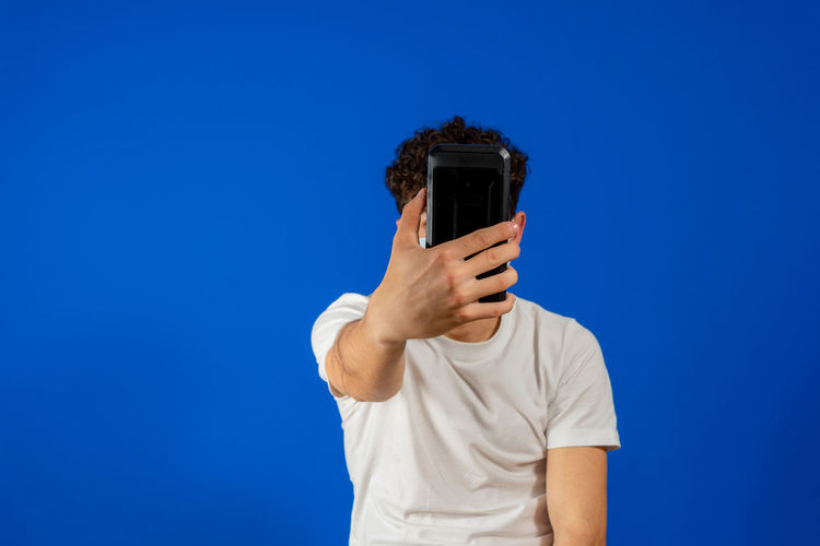 Low angle view of person holding smart phone against blue background