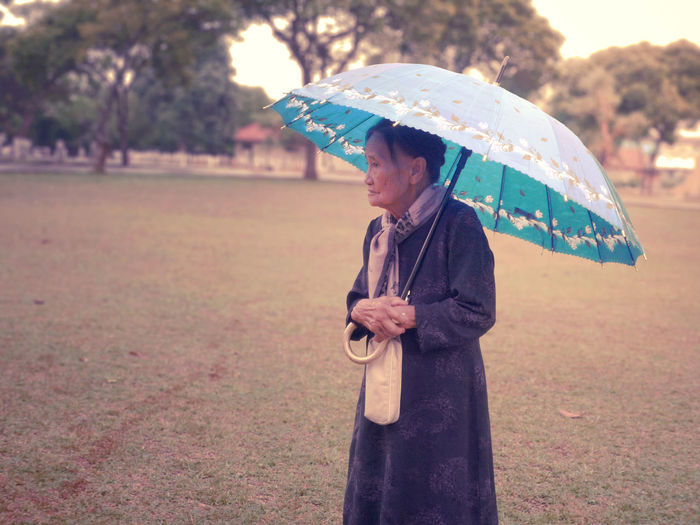 Senior woman carrying umbrella standing on field at park