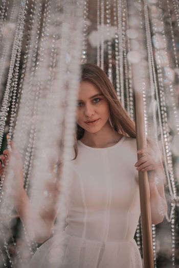 Portrait of beautiful young woman standing against curtain