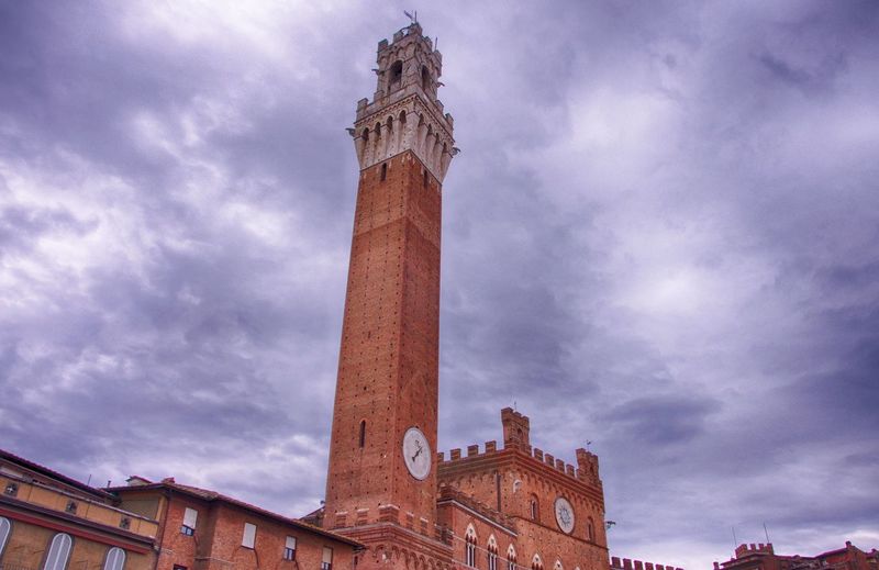 Low angle view of torre del mangia against cloudy sky in city