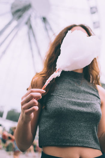 Woman with cotton candy against ferris wheel at amusement park