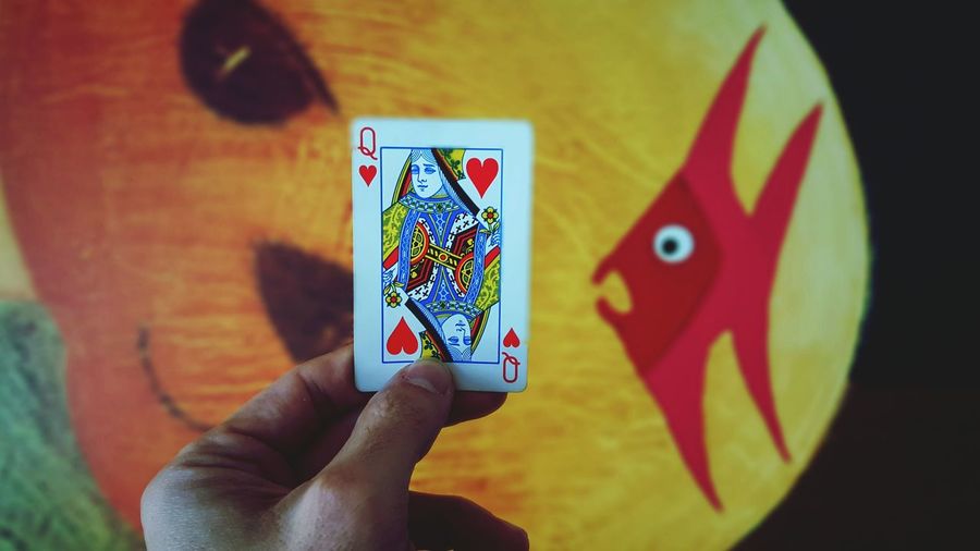 Cropped image of hand holding queen of hearts against wall
