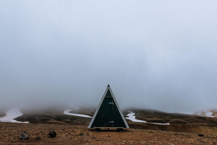 Triangle shape outhouse on ground during foggy weather