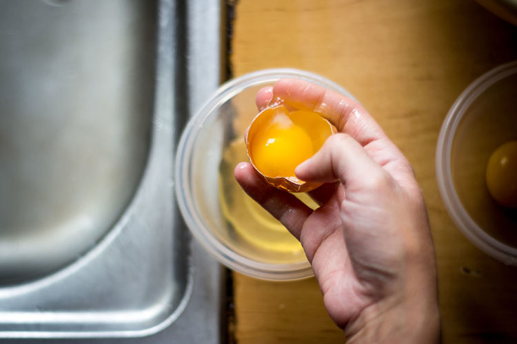 Cropped image of hand holding broken egg in kitchen