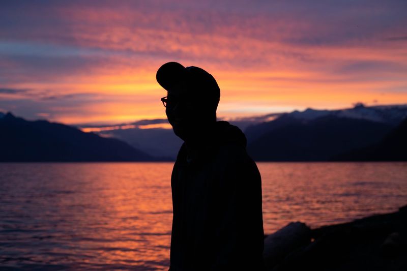 Silhouette man standing by sea against orange sky