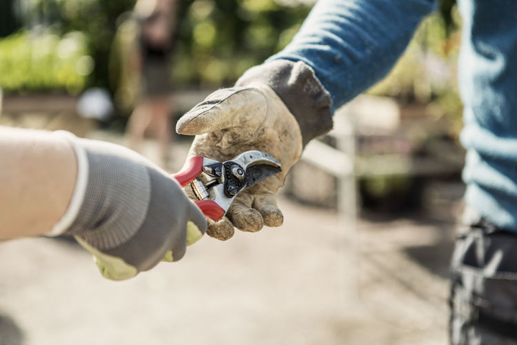 Cropped image of woman giving pliers to man at community garden