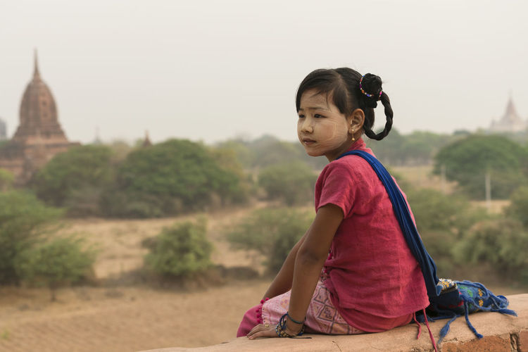 Girl painted face sitting on retaining wall against historic temple