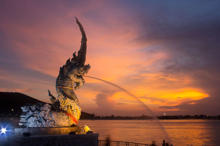 Illuminated naga statue by songkhla lake against sky at dusk